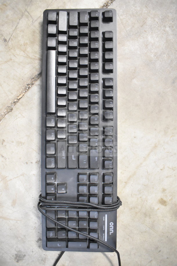 A black ONN wired keyboard on a concrete surface, cable wrapped around it.