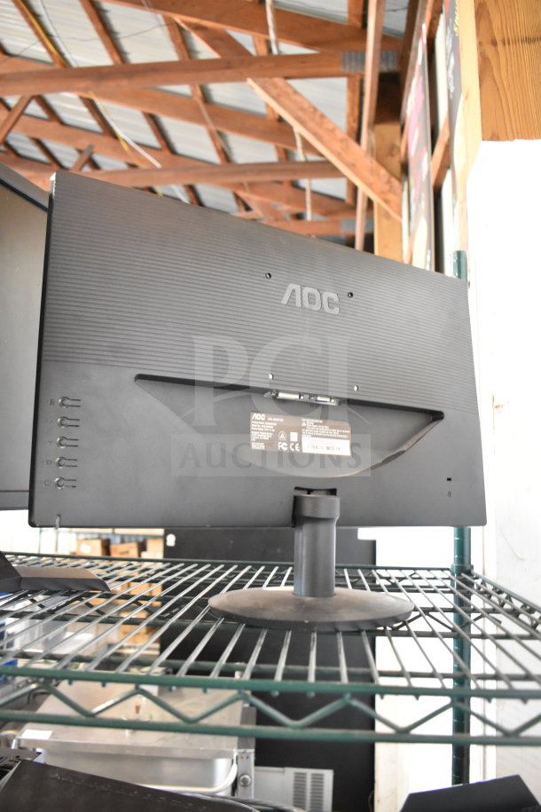 Four monitors including AOC and other brands, mounted on a wire shelf. Some labels visible, indicating model and specifications.