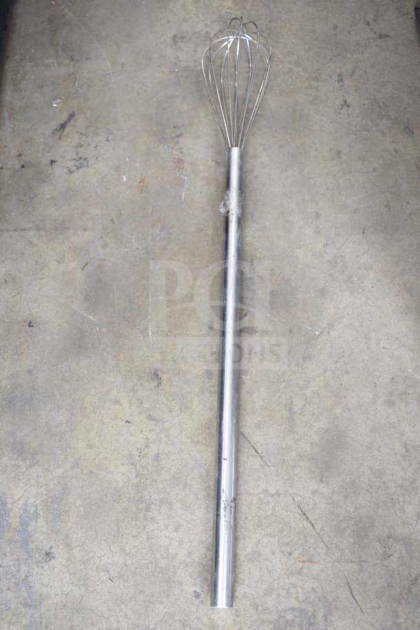Large industrial whisk with metal handle and wire loops, showing signs of wear but in functional condition.