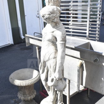Stone garden statue depicting a draped figure holding a jar, with ornate vase atop. Weathered condition, detailed carvings.