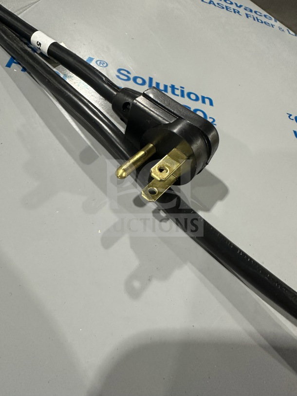 Close-up of a black power cord with a three-prong plug on a grey surface.