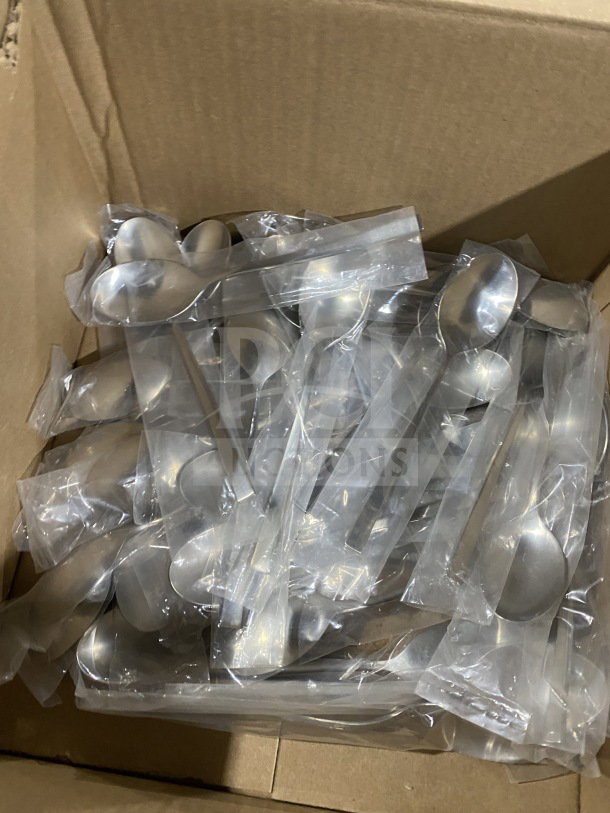Box of brand-new commercial stainless steel teaspoons in plastic wrappers, indicating pristine condition.