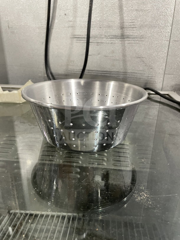 Brand new commercial 1/3" aluminum colander on a glass surface, showcasing perforated design. Ideal for bulk cooking.