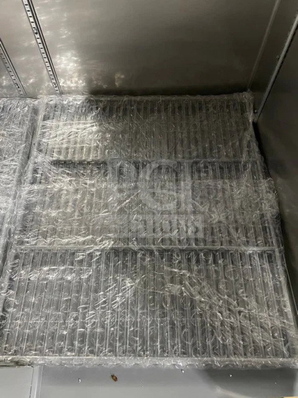 Alt text: Stainless steel reach-in refrigerator interior, featuring poly-coated wire racks wrapped in plastic.