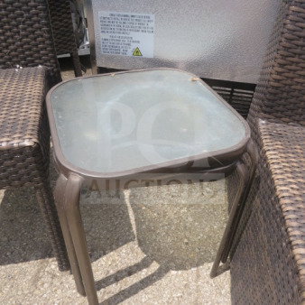 Woven wicker side table with glass top, brown finish, used condition, visible scratches. Suitable for outdoor use.