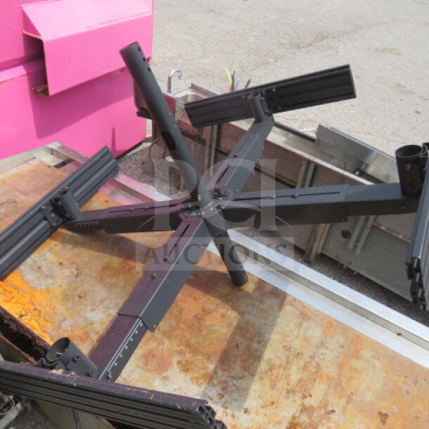 Black metal TV mount for four TVs, shown on flat surface. Appears sturdy with adjustable arms, suitable for multiple screens.