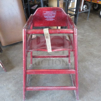 Wooden high chair with safety straps, red finish, visible caution label, sturdy frame, used condition.