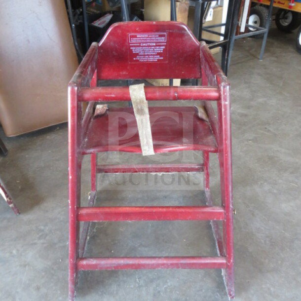 Red wooden high chair with safety straps, visible wear, caution label on backrest, classic design, sturdy construction.