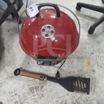 Red tabletop portable grill with vented lid and handle, accompanied by a black and orange spatula. Auction tag "78R" visible.