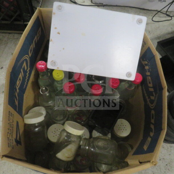 Cardboard box containing assorted glass bottles and jars with colored caps in various sizes and conditions.