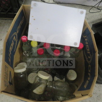 Cardboard box containing assorted glass bottles and jars with colored caps in various sizes and conditions.