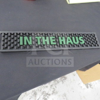 Black rubber bar mat with raised text "IN THE HAUS" in green. Rectangular with textured surface. Good condition.