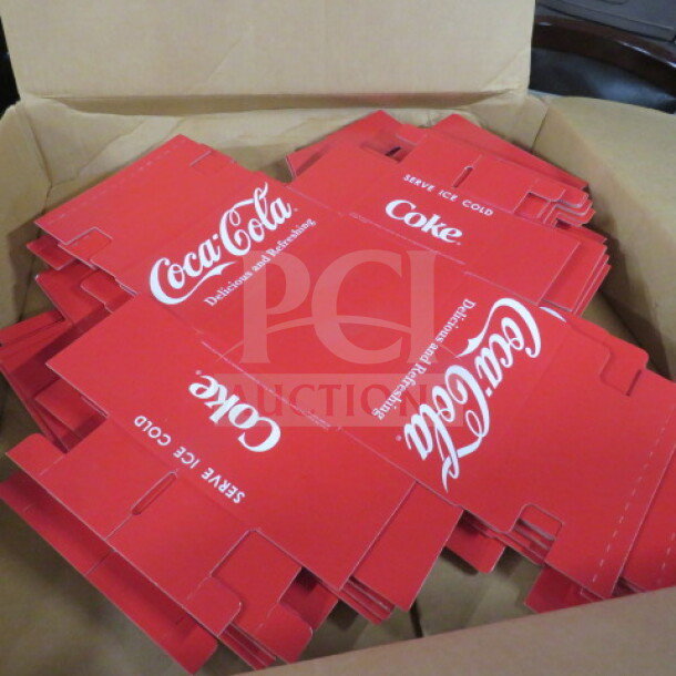 Box containing a lot of Coca Cola cardboard caddies, featuring the brand's logo and "Delicious and Refreshing" slogan, red color.