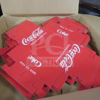 Box containing a lot of Coca Cola cardboard caddies, featuring the brand's logo and "Delicious and Refreshing" slogan, red color.