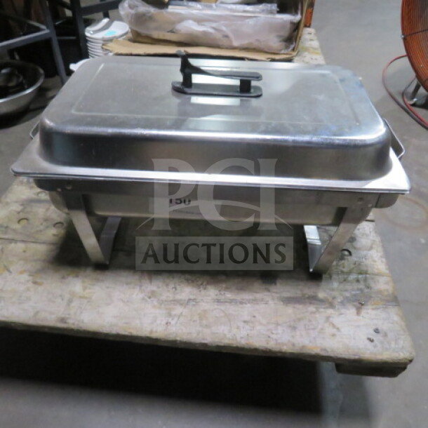 Full-size stainless steel chafer with lid, rectangular, handle on top, sits on a wooden surface, tag with number 150 visible.