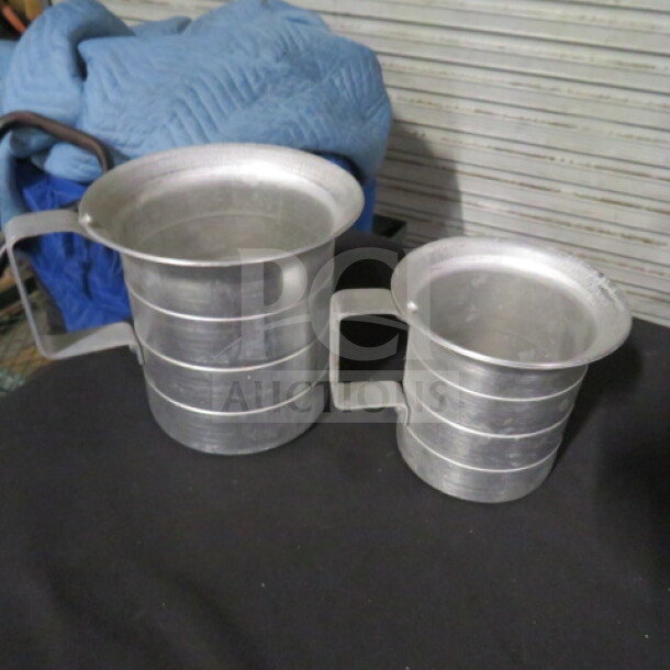 Assorted size aluminum measurer set with handles, in good condition. Includes two measuring cups with visible measuring lines.