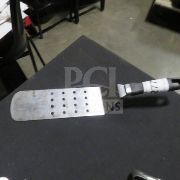 Perforated hamburger turner with metal blade and black handle, featuring multiple holes for drainage. Good condition.