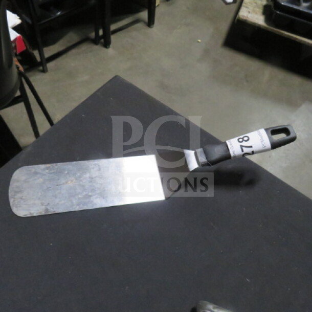 Stainless steel hamburger turner with black ergonomic handle, slight wear visible, auction tag reads "178."