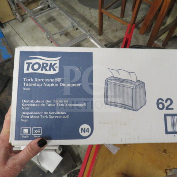 Brand new Tork Xpressnap tabletop napkin dispenser in box. Black color, model N4, includes 4 plastic dispensers.