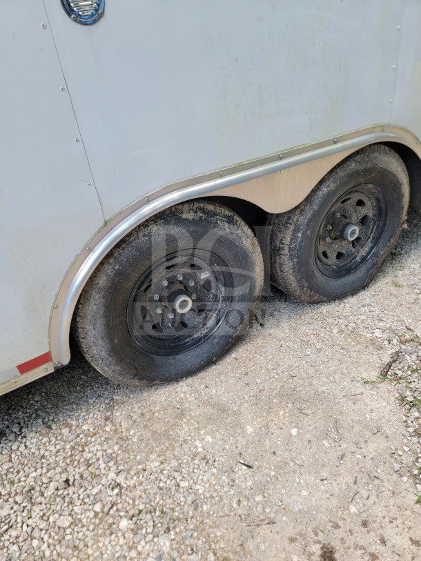 2021 Diamond Cargo 8.5' x 24' trailer wheels, tandem-axle, black rims, slightly worn, on gravel surface.