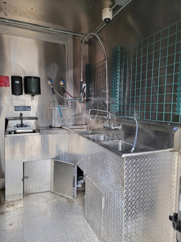 Interior of a 2021 Diamond Cargo mobile kitchen trailer with stainless steel sink, faucet, and metal diamond plate flooring.