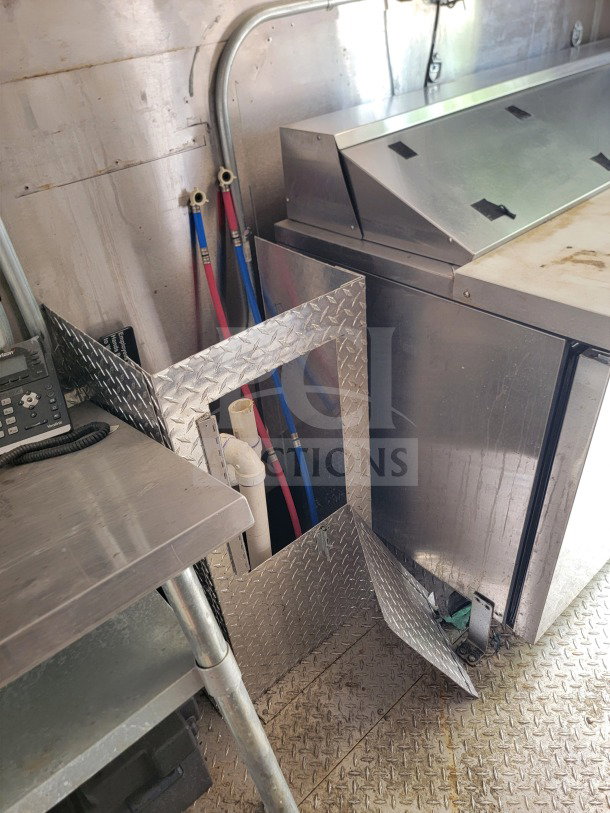 Interior of 2021 Diamond Cargo mobile kitchen trailer, featuring stainless steel surfaces, diamond plate flooring, and plumbing fixtures.