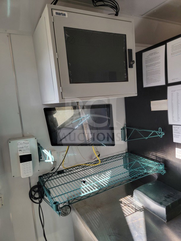 Mobile kitchen trailer interior featuring a Martin cabinet, monitor, metal wire shelf, and documents. Wiring visible.