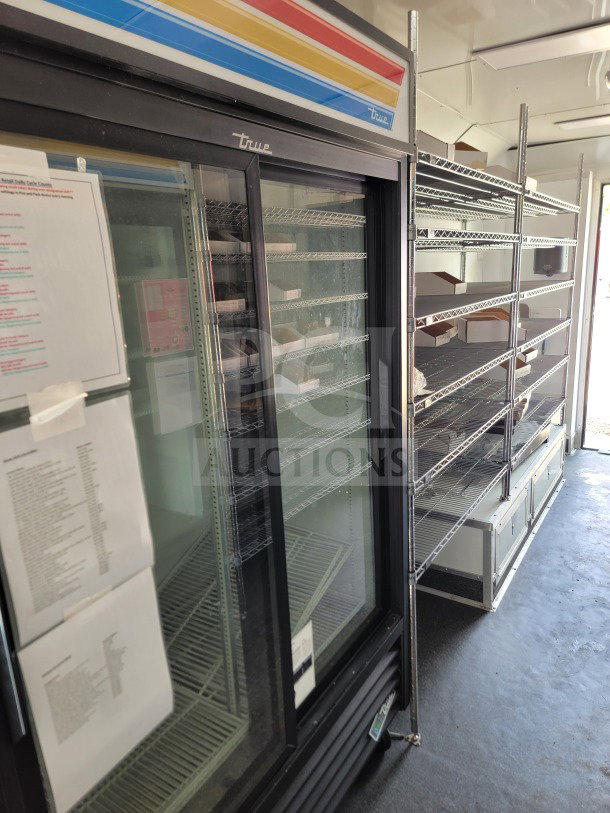 Alt text: Interior of SDG 8.5' x 20' mobile kitchen trailer, featuring True refrigeration unit and wire shelving.