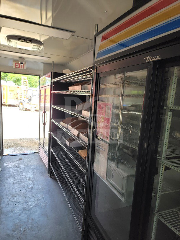 Interior of 2021 SDG 8.5' x 20' mobile kitchen trailer, featuring True refrigeration, wire shelving, and exit door.