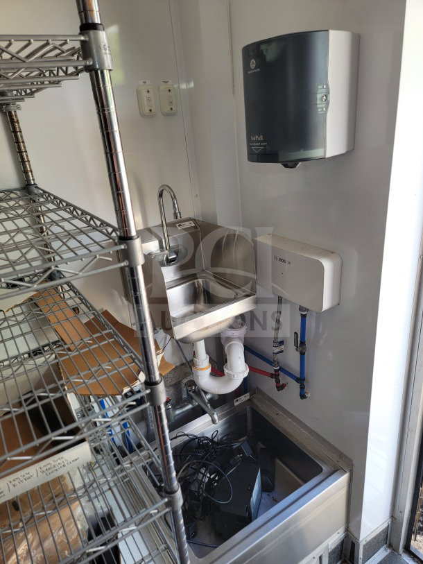2021 SDG 8.5' x 20' mobile kitchen trailer interior, featuring a stainless steel sink, storage shelves, and paper towel dispenser.