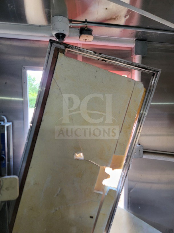 An interior view of a 2021 Rock Solid Cargo mobile kitchen trailer showing insulation damage and wiring, under a steel ceiling with a security camera.