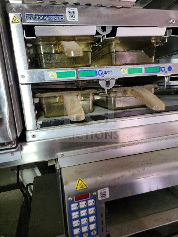Prince Castle commercial kitchen equipment with dual trays and control panel, visible heating warning label, part of a mobile kitchen trailer.