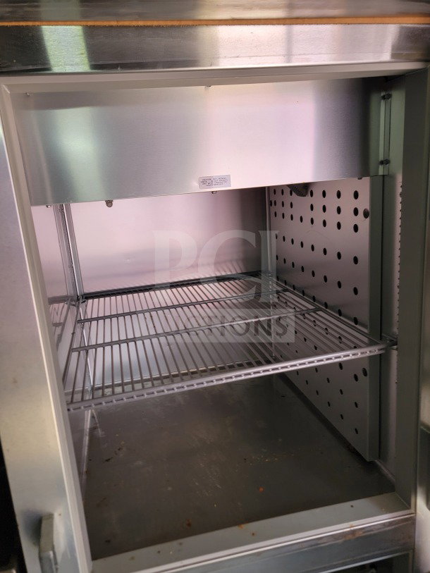 Interior view of a stainless steel refrigeration unit with wire racks, part of a Rock Solid Cargo mobile kitchen trailer.
