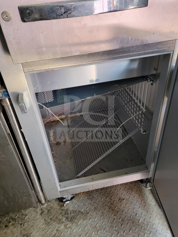 Open stainless steel refrigeration unit inside a mobile kitchen trailer, showing wire shelving and moderate interior wear.