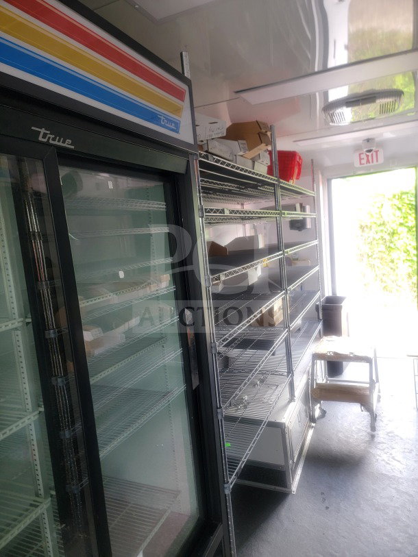 2021 SDG 8.5' x 20' dual-axle trailer interior, featuring True glass-door refrigeration, metal shelving, and storage area.