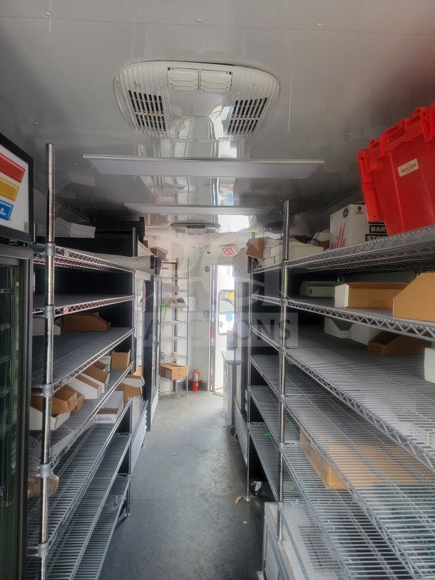 Inside view of 2021 SDG 8.5' x 20' dual-axle trailer, featuring shelving and True glass-door refrigeration.