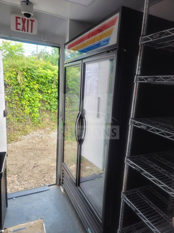 8.5' x 20' SDG mobile trailer interior with True glass-door fridge, metal shelving, and exit sign. Dual-axle, for retail use.