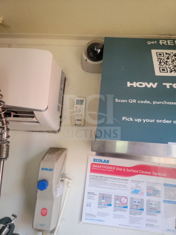 Interior view of a mobile kitchen trailer showing Ecolab sanitizer dispenser, instruction poster, and a wall-mounted AC unit.