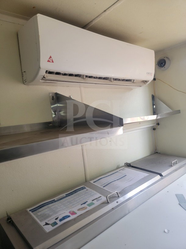 Interior view of a 2021 Rock Solid Cargo mobile kitchen trailer, showing upper stainless steel shelves and a white air conditioning unit.