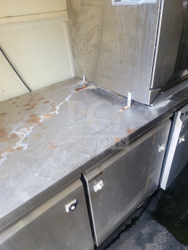 Stainless steel kitchen counter in a 2021 Rock Solid Cargo mobile trailer, showing signs of use with stains and marks.