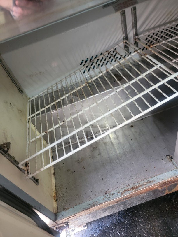 Interior view of Serv-Ware refrigeration unit from a 2021 Rock Solid Cargo trailer, showing wire shelves and signs of wear.