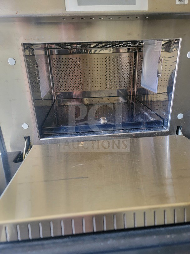 Interior view of stainless steel appliance, showing perforated metal walls and pull-out shelf, indicative of commercial kitchen use.