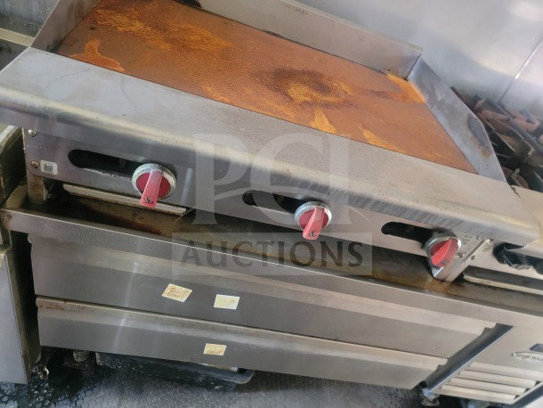 Griddle with rusted surface in a 2021 Rock Solid Cargo 8.5' x 24' mobile ghost kitchen trailer; features three red knobs.