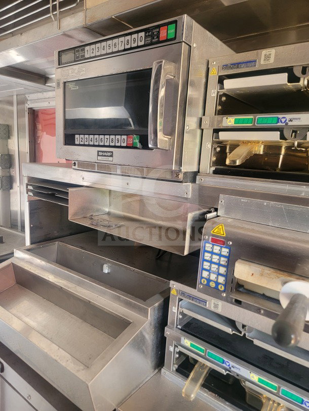 Mobile QSR kitchen trailer interior: Sharp microwave, Prince Castle units, durable stainless steel setup for high-volume food service.