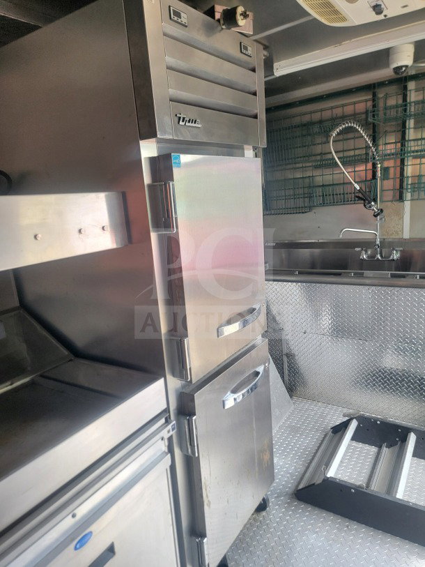 2021 Titanium Cargo 8.5' x 24' dual-axle kitchen trailer interior with True refrigeration, diamond plate floor, and sink.