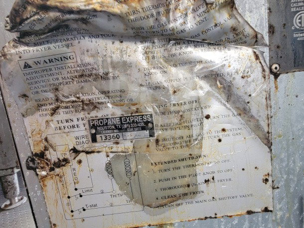 Corroded instruction panel with warning labels and "Propane Express" tag on a Diamond Cargo mobile kitchen trailer.