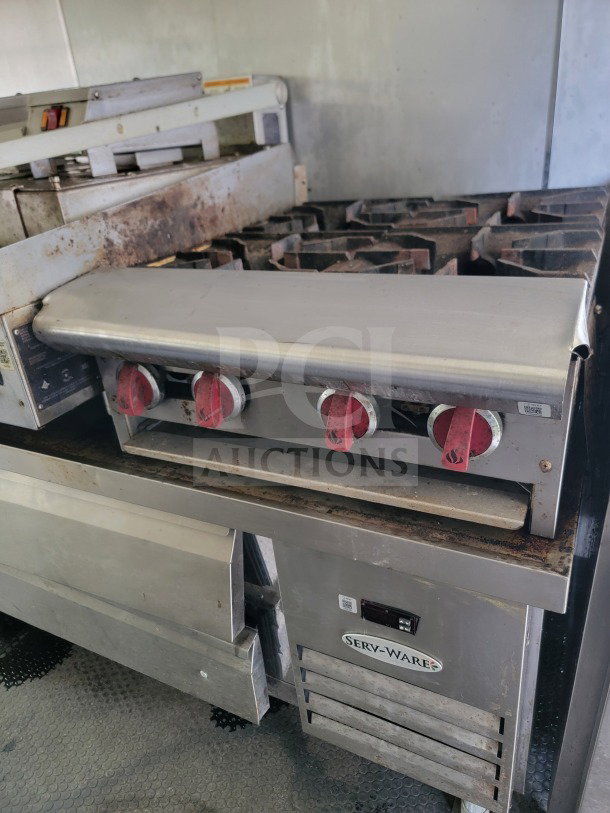 Serv-Ware commercial stove inside Diamond Cargo trailer, showing four red knobs and grills. Used condition, visible wear.