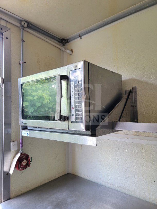 Commercial kitchen interior with an Amana microwave, mounted on a metal shelf. Fire safety system present. Clean condition.