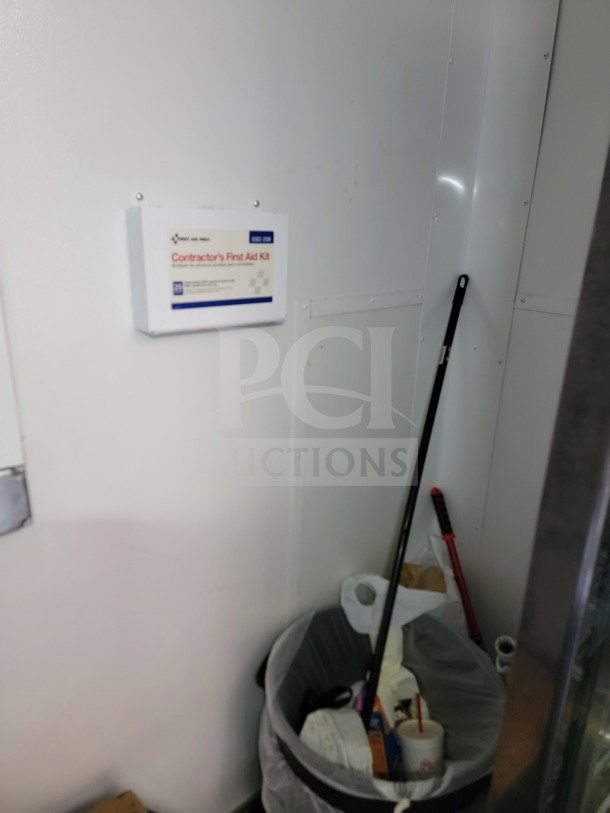 Interior of SDG 26 trailer showing a Contractor's First Aid Kit on the wall and a trash bin with cleaning tools nearby.