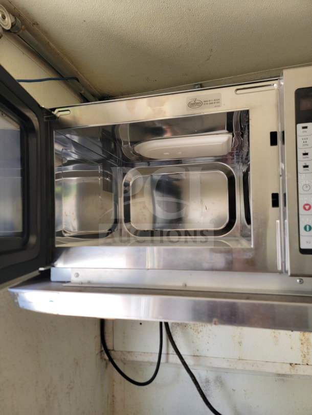 Interior of commercial microwave oven in Diamond Cargo mobile kitchen trailer; open door, visible steel lining.